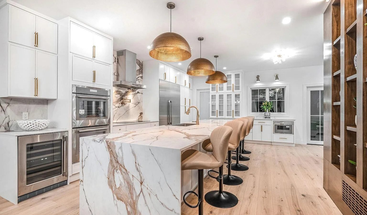 Kitchen with marble waterfall island, brass pendant lights and white cabinets