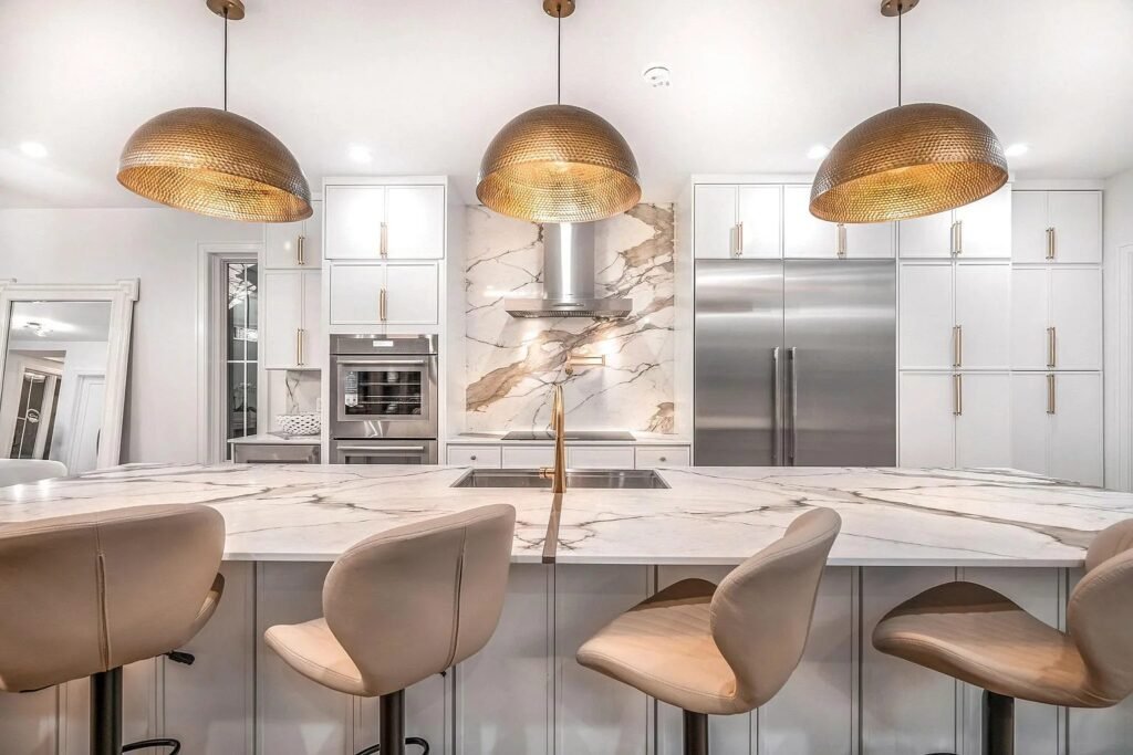 Large kitchen island with veined marble top and counter stools under brass pendants