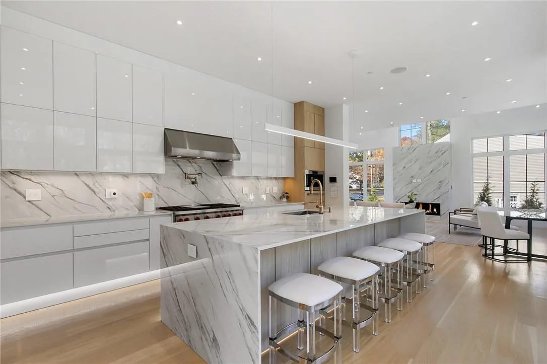 Modern white kitchen with long marble waterfall island and range hood